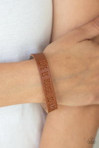 Life is Tough - Brown - Paparazzi Accessories -  Item #P9WD-URBN-563XX A dainty brown leather band is stamped in the phrase, "Life is tough. So Are You.," creating an inspiring centerpiece around the wrist. Features an adjustable snap closure.  Sold as one individual bracelet.