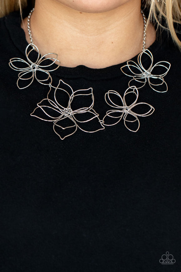 Flower Garden Fashionista - Silver - Paparazzi Accessories -  Item #P2ST-SVXX-173XX Shiny silver wire delicately twists into oversized blossoms. Varying in size, the airy floral frames delicately link into an asymmetrical display as the layered frames elegantly pop beneath the collar. Features an adjustable clasp closure.  Sold as one individual necklace. Includes one pair of matching earrings.