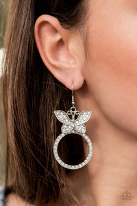 Paradise Found - White - Paparazzi Accessories -  Item #P5ST-WTXX-048XX A white rhinestone encrusted silver butterfly flutters atop a silver ring dotted in matching white rhinestones, resulting in a dazzling statement piece. Earring attaches to a standard fishhook fitting.  Sold as one pair of earrings.