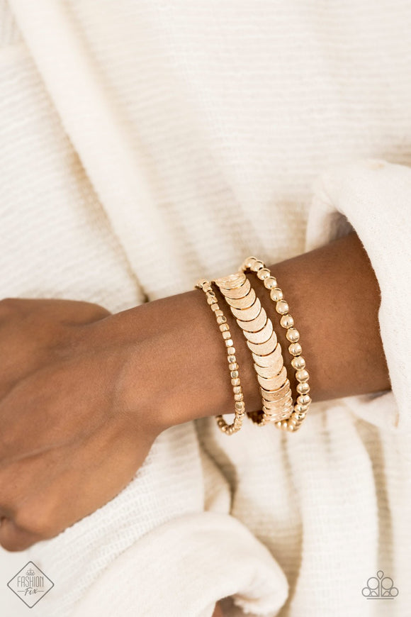 LAYER It On Me - Gold Bracelet - Sunset Sightings   Featuring rounded, cubed, and half-moon shapes, dainty gold beads are threaded along three different stretchy bands, creating trendy metallic layers around the wrist.  Sold as one set of three bracelets.