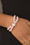 PAPARAZZI ACCESSORIES - Romantic Redux - Pink Joined at the center by an over-sized pink pearl and a pair of white rhinestone encrusted rings, classic pink pearls are threaded along stretchy bands around the wrist for a timelessly layered look.  Sold as one individual bracelet.