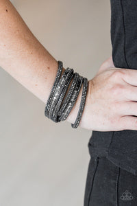 PAPARAZZI ACCESSORIES - Rock Star Attitude - Dark Gray - Paparazzi Accessories  Encrusted in rows of glittery hematite rhinestones and flat gunmetal and silver studs, three strands of gray suede wrap around the wrist for a sassy look. The elongated band allows for a trendy double wrap around the wrist. Features an adjustable snap closure.  Sold as one individual bracelet.