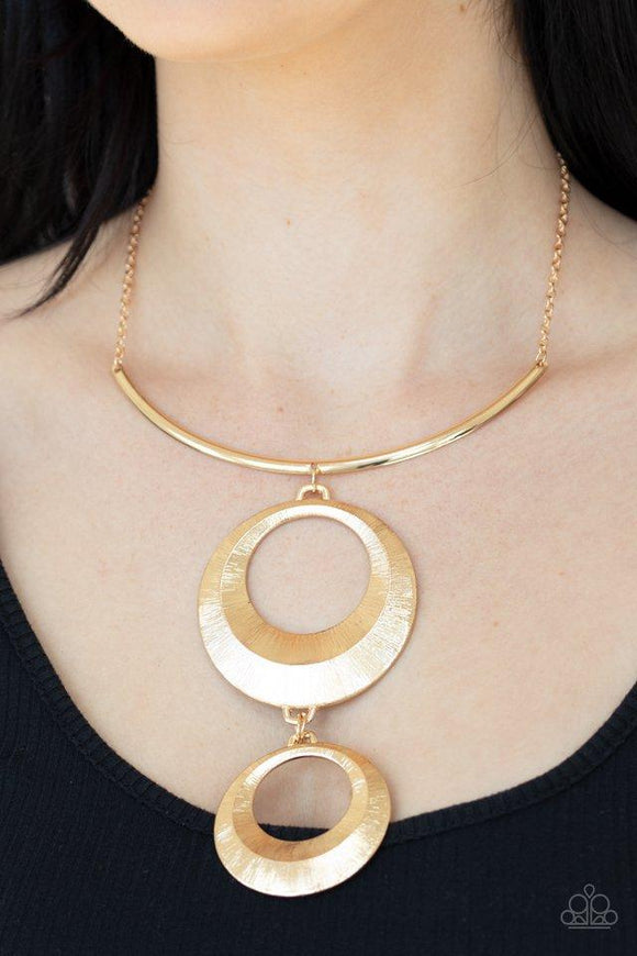 Egyptian Eclipse - Gold - Paparazzi Accessories  Featuring a blinding scratch finish, two beveled gold circular frames swing from the bottom of a bowing gold rod, creating an edgy stacked pendant down the chest. Features an adjustable clasp closure.  Sold as one individual necklace. Includes one pair of matching earrings.